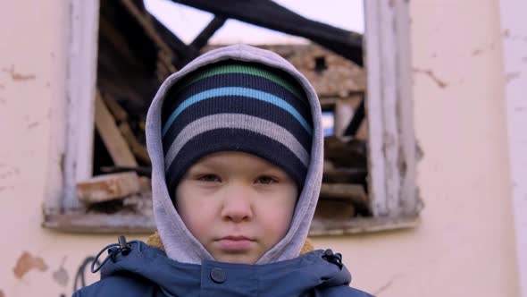 Hungry Homeless Boy Looks at the Camera Against the Background of the Ruins