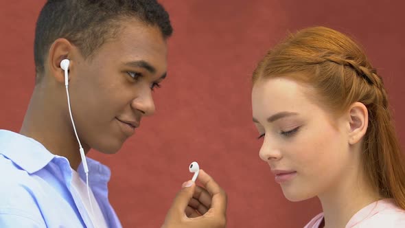 Enamored Male Teen Giving Earphone to Young Girl, Listening to Music Together