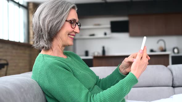 Mature Senior Woman is Using a Smartphone at Home