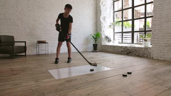 A Boy Hockey Player Trains with a Hockey Stick and Puck on a Slippery Surface Indoors. Slow Motion