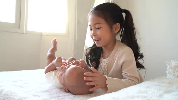 Asian Family of Cute Little Sister Touching Newborn Baby Boy Brother on Bed