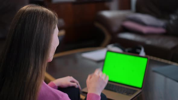 Shooting Over Shoulder of Slim Caucasian Young Woman Waving at Video Chat on Blurred Laptop with