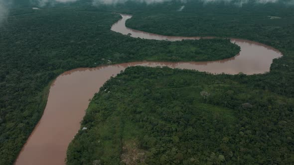 Aerial tilt up shot showing tranquil brown colored Amazon River floating between jungle of South Ame