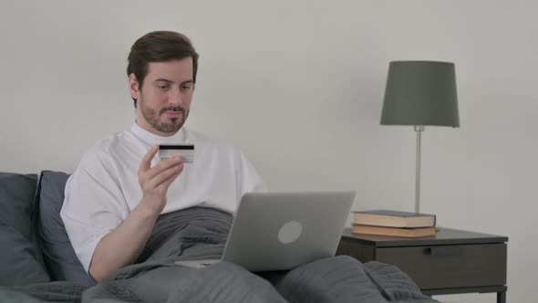 Young Man Making Online Payment on Laptop in Bed