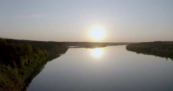 sunset along a large wide river around the forest and fields. drone