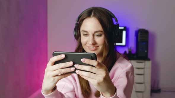 Cute Gamer Woman Sit on a Gaming Chair Smiling and Playing Mobile Online Game on a Smartphone