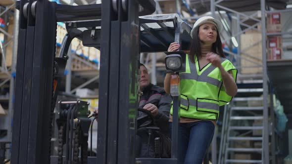 Portrait of Caucasian Woman in Hard Hat Standing on Forklift As Autoloader Operator Driving