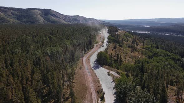 Multiple cars driving along a dusty logging road that leads through boreal forests near Ghost River,