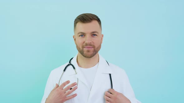 Successful Physician in White Lab Coat and Mask Looks at the Camera and Smiles on a Blue Background