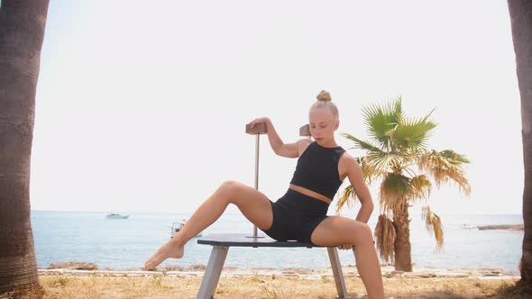 Young Blonde Female Gymnast Dancing By High Stands on the Beach