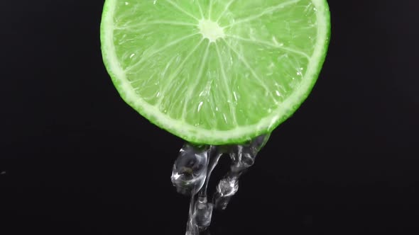 Water drops falling from juicy lime on black background. Lime slice and water splashing, drops