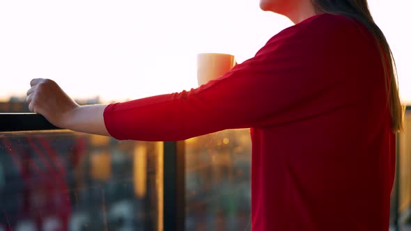 Woman in Red Dress with a Cup of Coffee Standing on the Balcony and Admire the Sunset