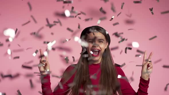 Red dressed excited girl with hat jumping, applauding, having fun, rejoices over confetti rain 