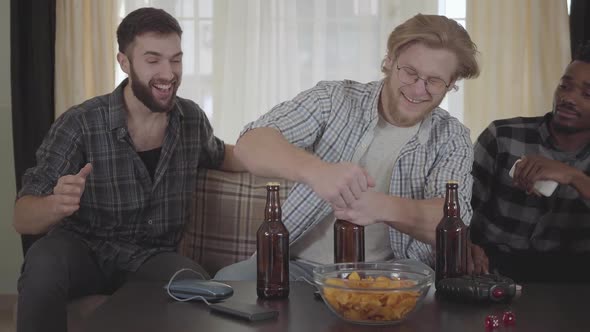 Three Young Happy Friends Drinking Beer and Talking at Home Together