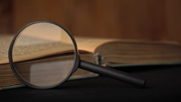 Girl Turns the Page of an Old Book Next to a Magnifying Glass