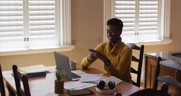 African american woman talking on smartphone and using laptop while working from home