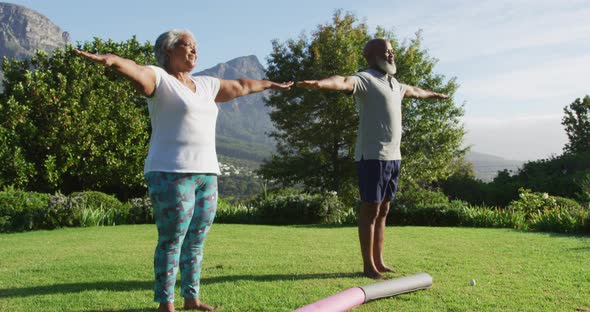 African american senior couple practicing yoga together while standing in the garden