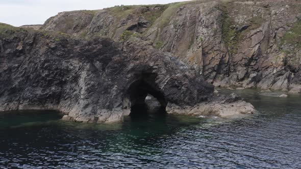 Aerial retreats from sea cave to reveal green cliff top countryside