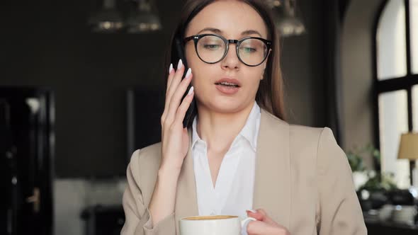 Business Woman in Eyeglasses Having Mobile Phone Call Holding Coffee in Cafe