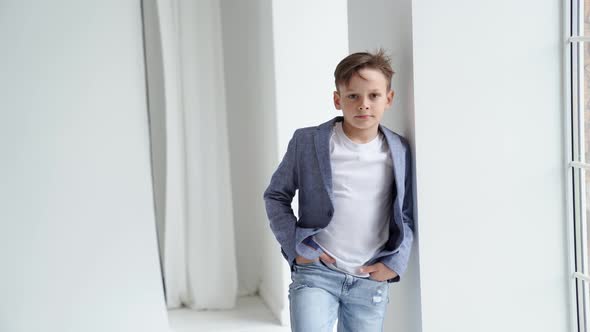 A Teenage Boy in a Jacket and Jeans Poses Standing By a Window