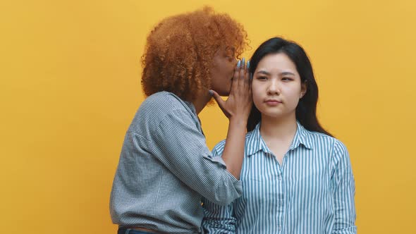 Young African American Black Woman Whispering To Her Asian Friend Expressing Shock