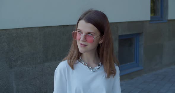 Portrait of Admiring Teen in Sunglasses Looks Aside Camera with Smile Outdoors