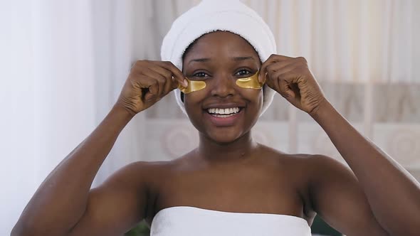 Young African Woman Smiling While Removes Medical Golden Patches in Bedroom