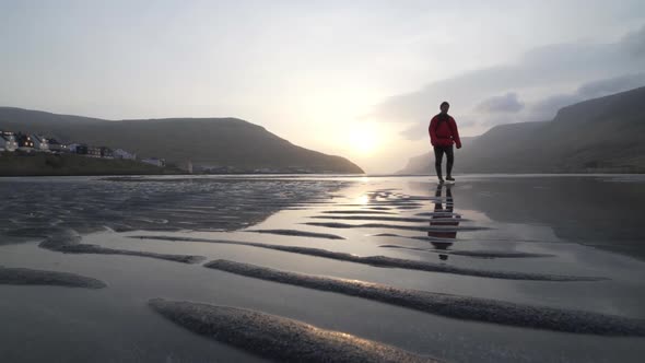 Man Waking Through Shallow Waters And Sand At Sunrise