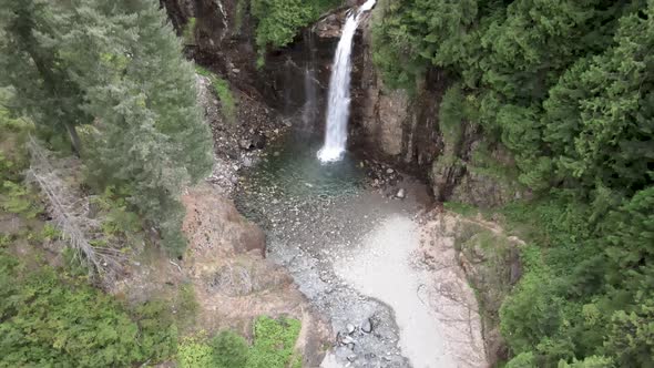 Water cascades over a hidden grotto nestled in lush evergreen forest, aerial reveal