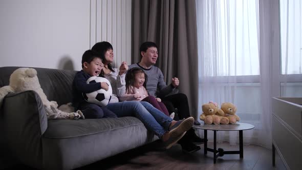 Cheerful Chinese Family Watching Soccer Game on TV