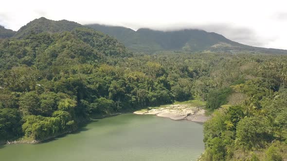 Aerial Panorama Tropical Forest on Lake Shore and Green Mountains in Cloudy Sky. Drone View Green