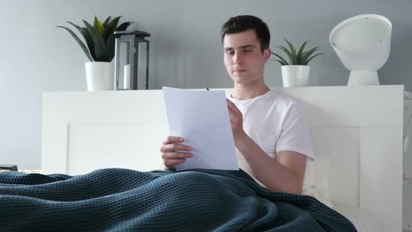 Man Reading Documents in Bed Paperwork
