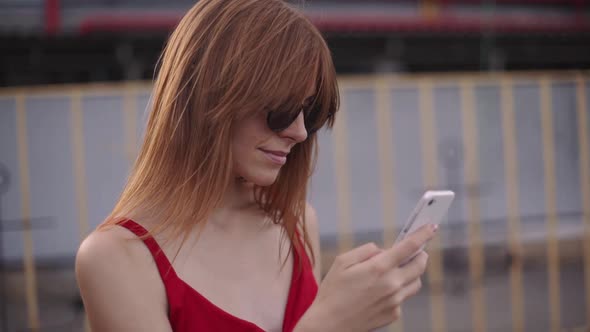 Portrait of Attractive Young Redhaired Woman on Street in Red Dress Use Smartphone