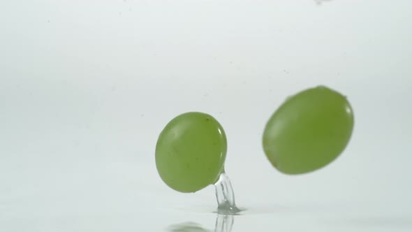 Green grapes falling and bouncing on water surface. Slow Motion.