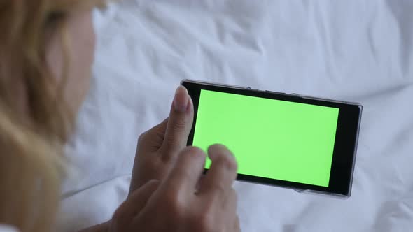 Woman holding greenscreen smartphone in the bed 4K 2160p 30fps UltraHD footage - Female blond  relax