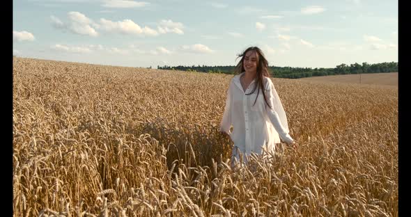 Young Brunette Woman in White Clothes Walking in a Wheat Field