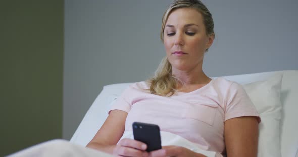 Caucasian female patient lying in hospital bed and using smartphone