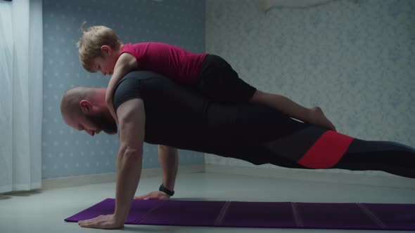 Bearded 30s father in sportswear making push ups exercise with young son on his back