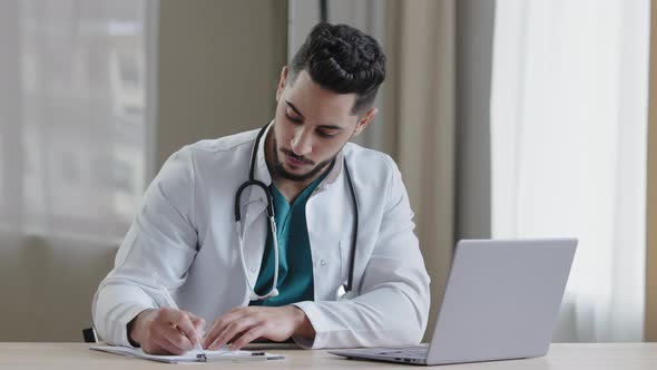 Concentrated Arabian Man Doctor Practitioner Sit at Clinic Cabinet Use Computer Chatting Distant in