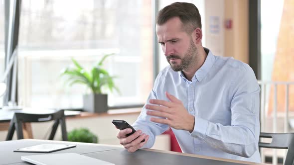 Young Man Reacting To Loss on Smartphone in Office 