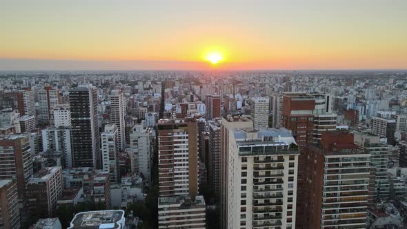 Dolly in flying over Buenos Aires city buildings at sunset with bright sun in horizon, Argentina