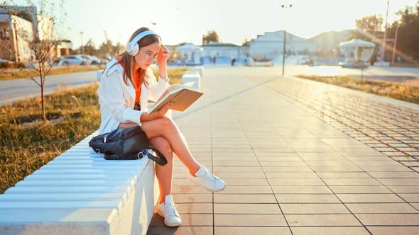 Teenage Girl Sitting on Park Bench and Reading Her Favorite Interesting Aloud Flipping Through Pages