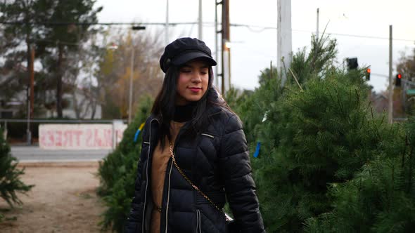 A hispanic woman shopping for a seasonal holiday Christmas tree decoration on a lot with many specie