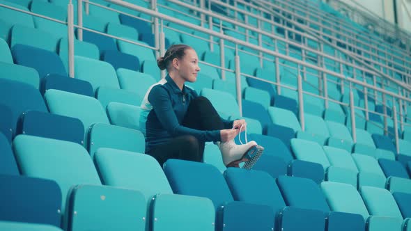 Young Girl is Lacing Up the Skates on the Seats of the Sports Arena