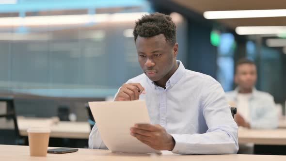 African Businessman Reacting to Loss While Reading Documents