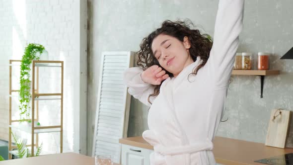 Sleepy Young Woman Stretching and Drinks a Glass of Water in Early Morning