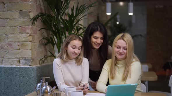 Front View of Positive Carefree Women Talking at Tablet Video Chat Sitting in Cafe Smiling and