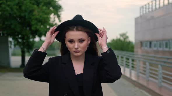 A Young Attractive Woman in a Hat is Walking Down a City Street