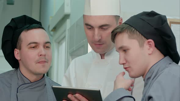 Concentrated Chef Showing His Trainees Something on Digital Tablet