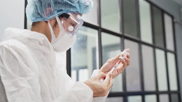 Asian male researcher doctor in PPE holding the COVID vaccine on laboratory before test on human.